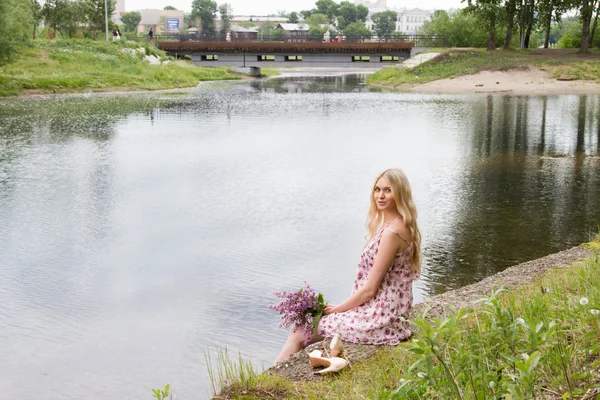 Молодая беременная женщина с букетом сирени на берегу реки — стоковое фото