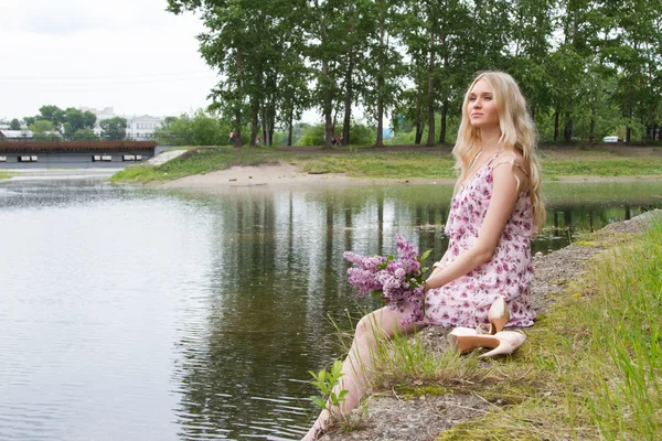 Jonge zwangere vrouw met een boeket van seringen aan de rivieroever — Stockfoto