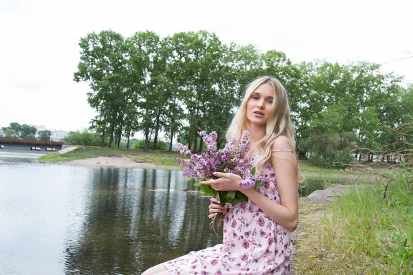 Mujer embarazada joven con un ramo de lilas en la orilla del río —  Fotos de Stock