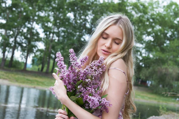 Jeune femme enceinte avec un bouquet de lilas sur la rive de la rivière — Photo