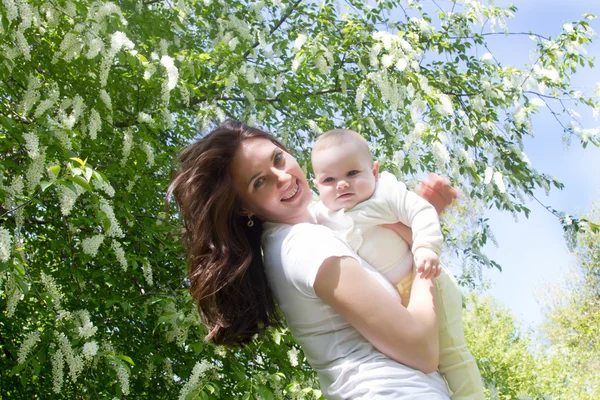 Happy mother with a baby on a background of a blossoming bird cherry — Stock Photo, Image