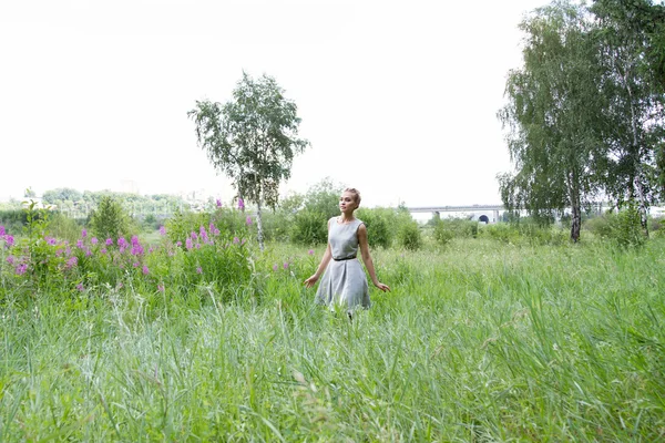 Girl goes on the field with tall grass and wildflowers — Stock Photo, Image