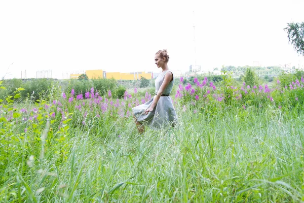 Meisje gaat op het veld met hoog gras en wilde bloemen — Stockfoto