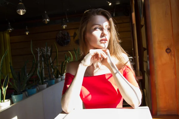 Девушка в красном платье сидит за столом у окна — стоковое фото