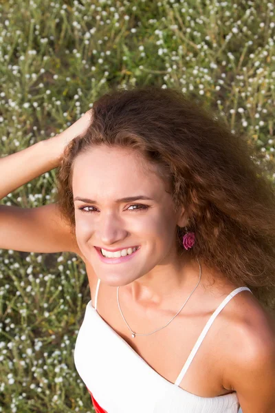 Krullend meisje op de achtergrond van wilde bloemen. Zomer portret. — Stockfoto