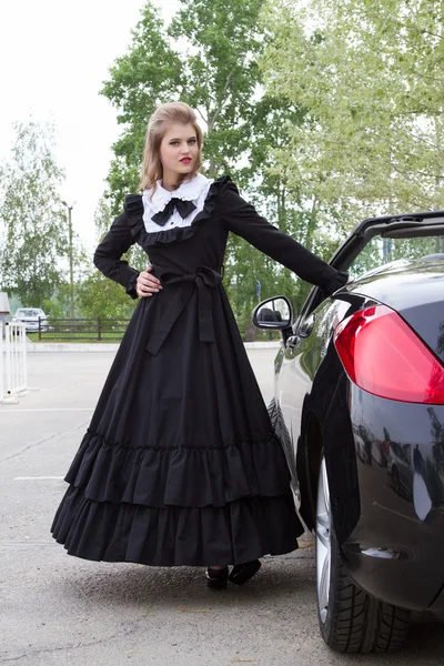 Meisje in oude lange jurk staande in de buurt van de moderne auto — Stockfoto