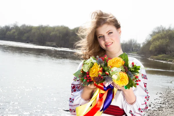 Niña en una camisa bordada y una corona de flores frescas en la orilla del río — Foto de Stock