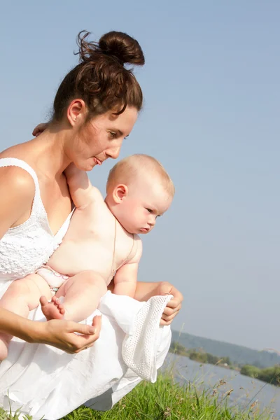 Mum with a small child sitting in the grass on the bank of the pond — Stock Photo, Image