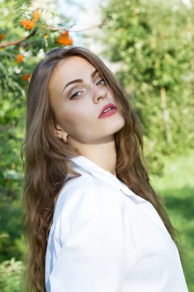 Chica joven con el pelo largo y una camisa blanca sobre un fondo del parque —  Fotos de Stock