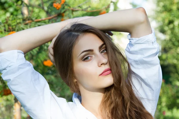 Chica joven con el pelo largo y una camisa blanca sobre un fondo del parque —  Fotos de Stock