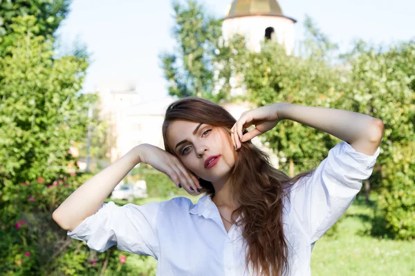 Chica joven con el pelo largo y una camisa blanca sobre un fondo del parque — Foto de Stock