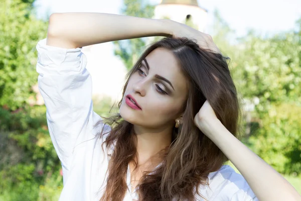 Chica joven con el pelo largo y una camisa blanca sobre un fondo del parque —  Fotos de Stock