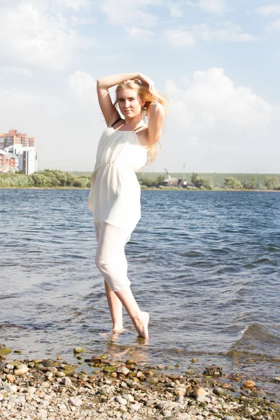 Blond meisje in een witte jurk aan de kust — Stockfoto