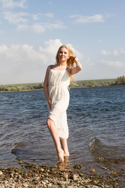 Blond flicka i en vit klänning på stranden — Stockfoto