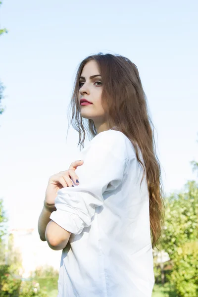 Beautiful young girl with long hair and wearing a white shirt in the summer park — Stock Photo, Image