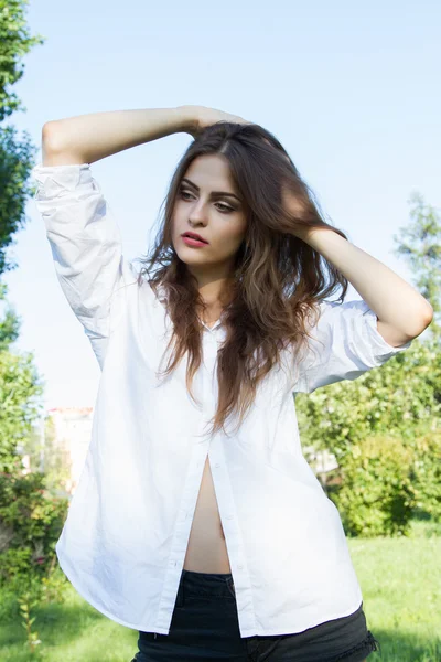 Beautiful young girl with long hair and wearing a white shirt in the summer park — Stock Photo, Image