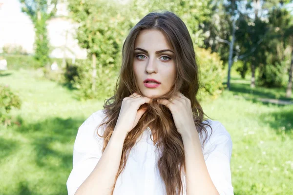 Szép fiatal lány hosszú hajjal és egy fehér inget visel, a nyári park — Stock Fotó