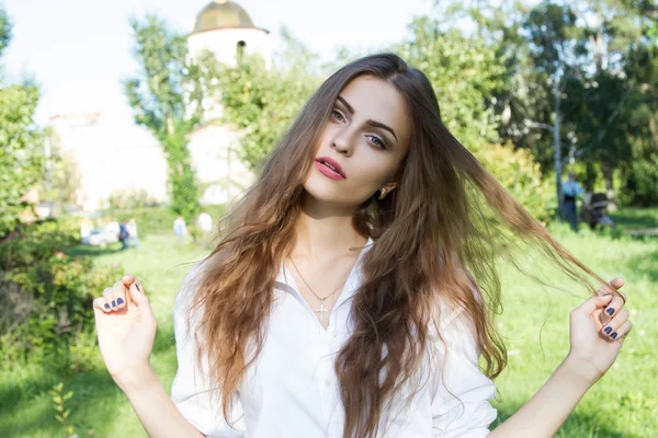 Όμορφη νεαρή κοπέλα με μακριά μαλλιά και φοράει ένα άσπρο πουκάμισο στο πάρκο καλοκαίρι — Φωτογραφία Αρχείου