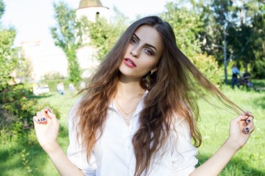 Uzun saçlı ve yaz parkta beyaz bir gömlek giymiş güzel genç kız