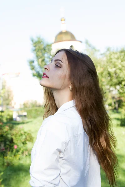 Красивая девушка с длинными волосами и в белой рубашке в летнем парке — стоковое фото