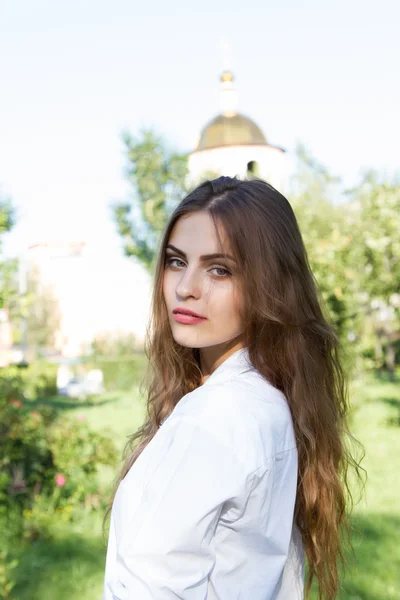 Szép fiatal lány hosszú hajjal és egy fehér inget visel, a nyári park — Stock Fotó