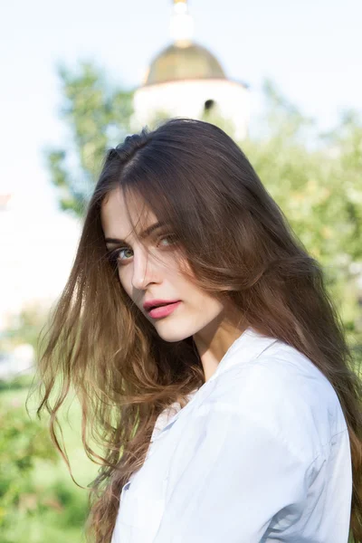 Beautiful young girl with long hair and wearing a white shirt in the summer park — Stock Photo, Image