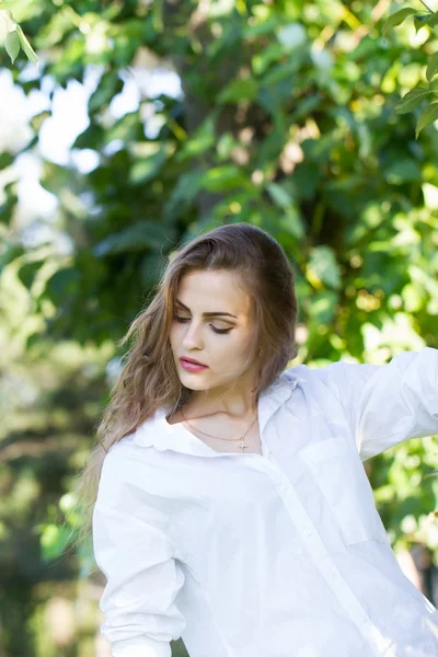 Vacker ung flicka i vit skjorta promenader i parken. — Stockfoto