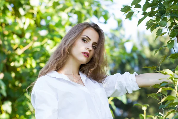 Schönes junges Mädchen in weißem Hemd, das im Park spaziert. — Stockfoto