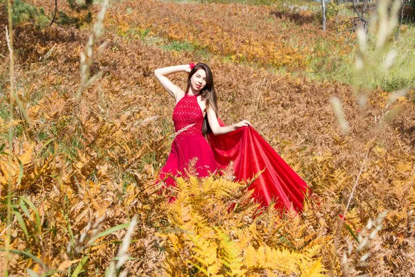 Mädchen im roten Abendkleid zwischen den gelben Blättern eines Farns — Stockfoto