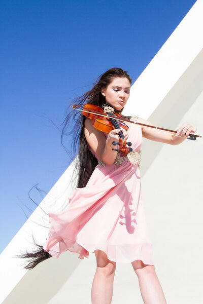 Violinist plays on the stage under the open sky in a pink dress