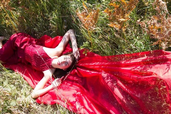 Mädchen im roten Abendkleid steckt im hohen Herbstgras — Stockfoto