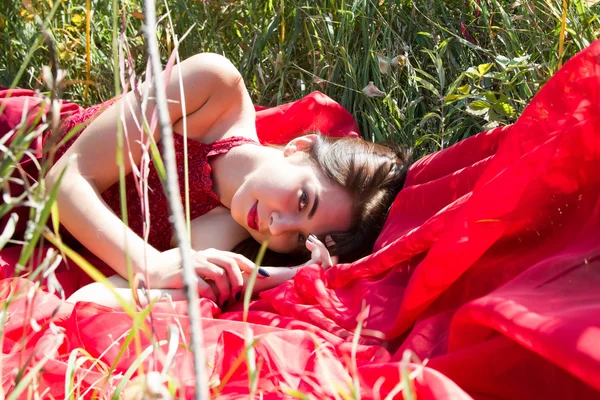 秋の芝生で横になっている赤いイブニング ドレスの女の子 — ストック写真