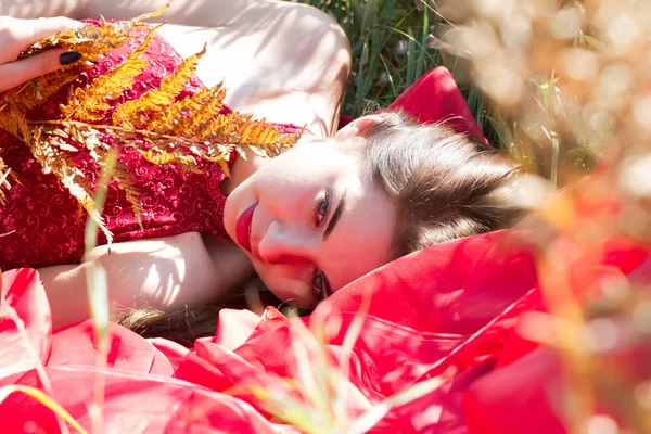 Mädchen in rotem Abendkleid liegt im Herbstgras — Stockfoto