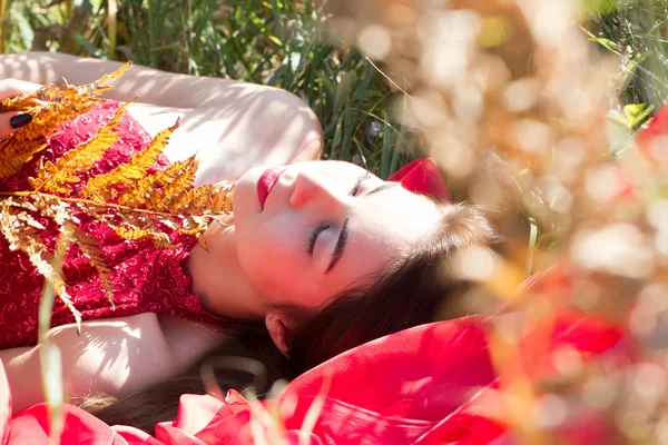 Girl in a red evening dress lying in autumn grass — Stock Photo, Image