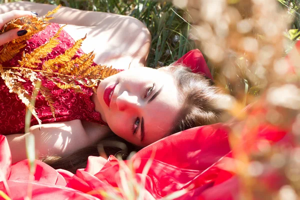 Girl in a red evening dress lying in autumn grass — Stock Photo, Image