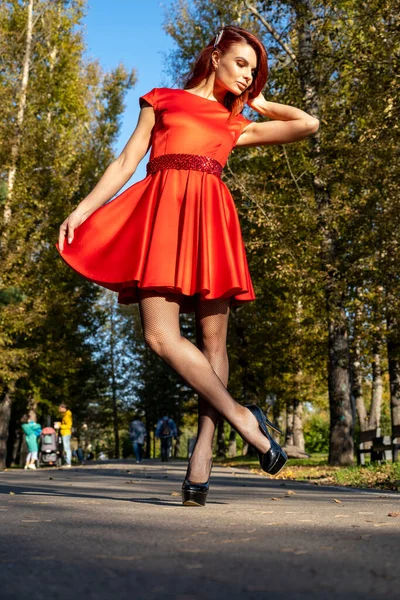 公園の路地にある短い赤いドレスの細い足の女の子 — ストック写真