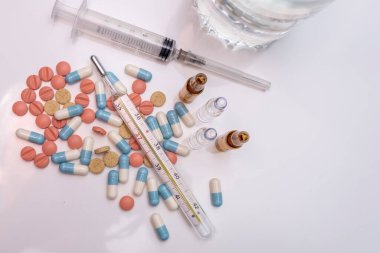 mercury thermometer lies on the table with pills and a syringe