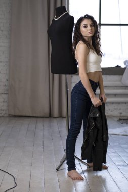 Kot pantolonlu ince bir kız odada bir mankenin yanında duruyor.