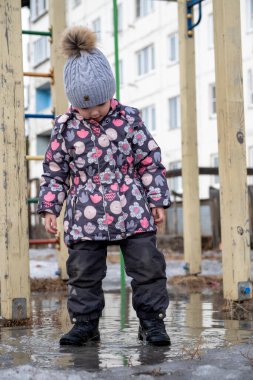 Küçük çocuk bahçede su birikintisinde duruyor.