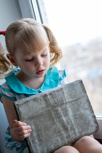 Küçük Kız Elinde Tabletle Pencere Eşiğinde Oturuyor — Stok fotoğraf