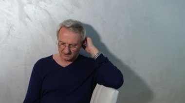 Akıllı telefon ekranına bakan yaşlı gri saçlı adam.