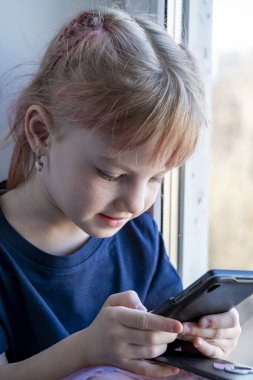 Çocuk pencere eşiğinde oturur ve akıllı bir telefonla oynanır.