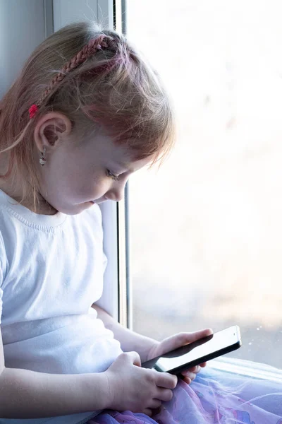 Çocuk Pencere Eşiğinde Oturur Akıllı Bir Telefonla Oynanır — Stok fotoğraf