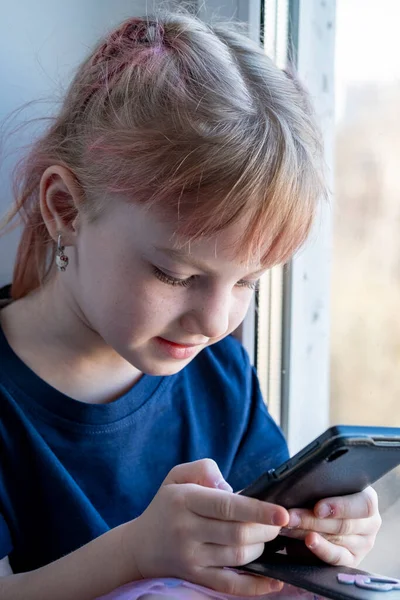 Çocuk pencere eşiğinde oturur ve akıllı bir telefonla oynanır.