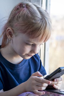 Çocuk cep telefonuyla pencere pervazında oturuyor