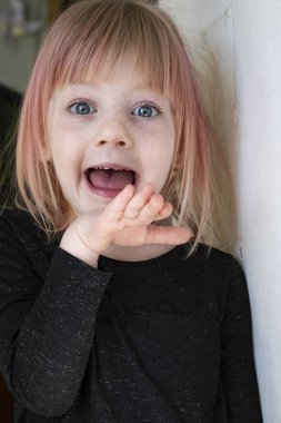 Yüzünde çiller olan küçük bir sarışın kameranın önünde surat yapıyor. Yakın plan portre.