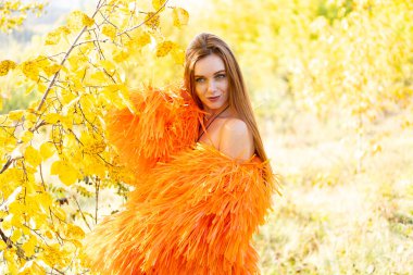 Sonbahar parkındaki kızıl saçlı genç kız sarı yaprakların ve çalıların arkasında