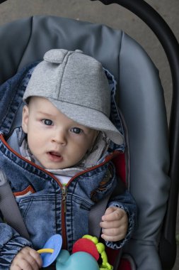 Küçük çocuk parkta bir bebek arabasında oturuyor.