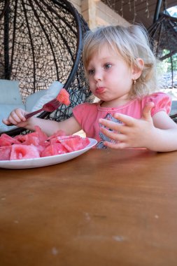 Küçük kız bir kır evinin verandasında karpuz yiyor.