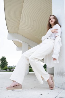 Beyaz elbiseli genç bir kız, arka planda aydınlık bir binanın arkasında